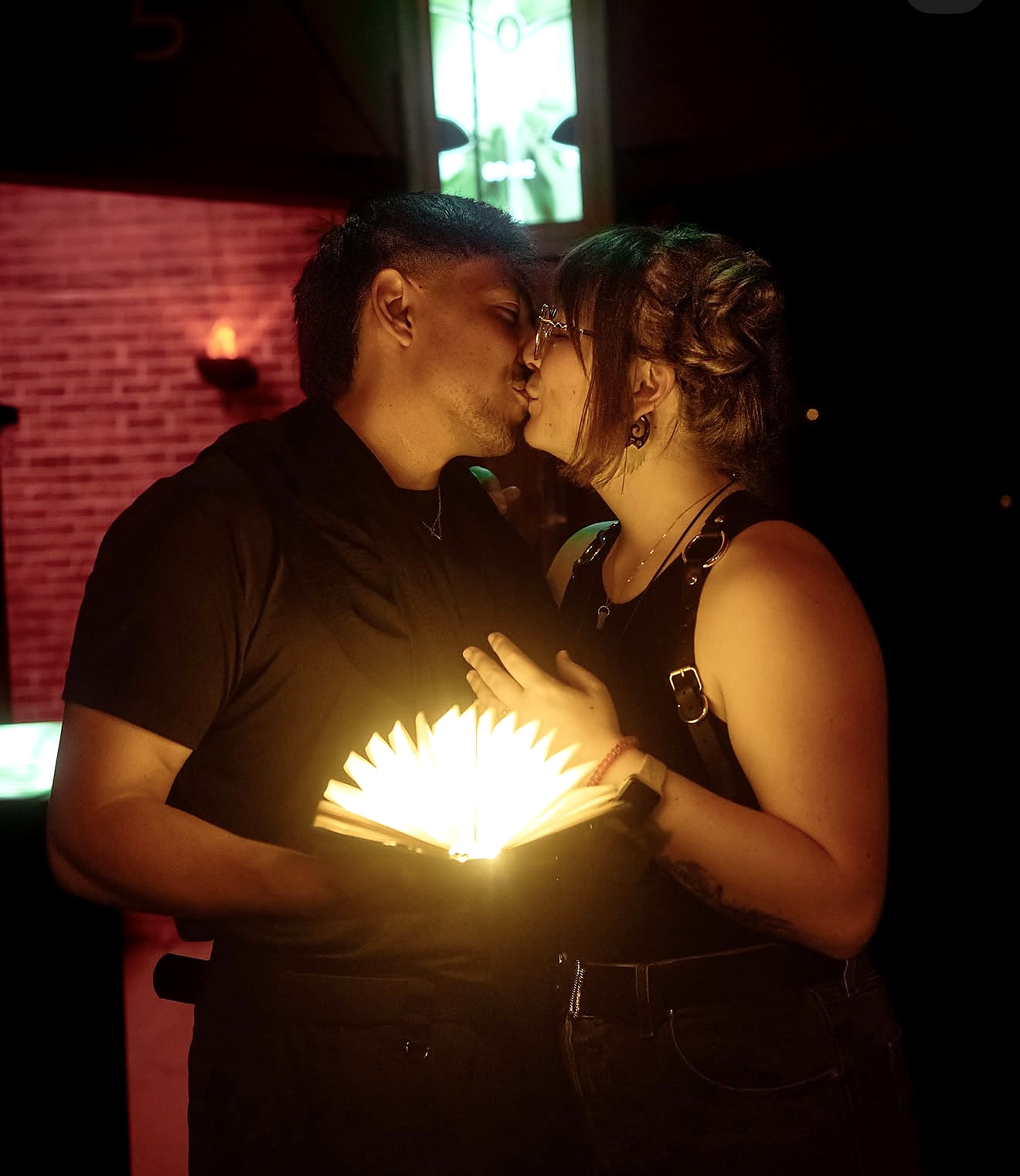 An engaged couple kissing over a glowing book